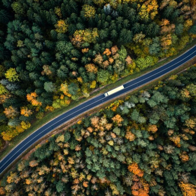 Arial view of heavy truck on a narrow twisting road. Autumn colorful trees by the sides of the road.