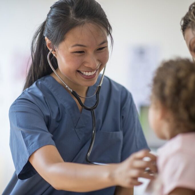 A nurse is listening to a little girl's heartbeat at a doctors appintment.